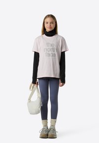 Jasnoróżowy bawełniany T-shirt z logo "the north face", noszony na czarnej bluzce z długim rękawem, zestawiony z ciemnymi legginsami i butami trekkingowymi.