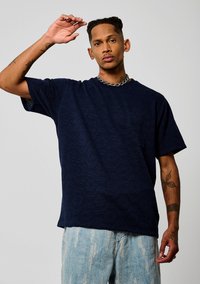 T-shirt à manches courtes bleu marine avec un motif hexagonal texturé, poche sur la poitrine gauche, coupe décontractée, associé à un jean délavé.