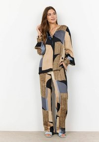 Tvådelad outfit med långärmad topp och vida byxor i abstrakta mönster av beige, svart och blå nyanser. Slät tygtextur.