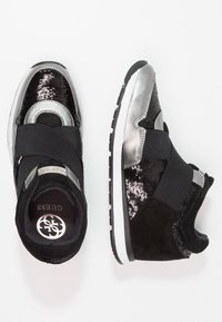 Czarno-srebrne sneakersy na koturnie z materiałem wyszywanym cekinami, elastycznym paskiem i gumową podeszwą. Gładkie i teksturowane powierzchnie podkreślają design.