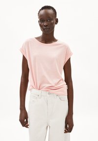 Ljusrosa t-shirt med kort ärm, rund hals och knutdetalj i midjan, tillsammans med högmidjade vita jeans. Slät tygyta.