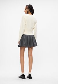 Suéter branco de malha combinado com uma saia plissada cinza. A saia apresenta um padrão de riscas e termina acima dos joelhos. Sapatos pretos completam o visual.