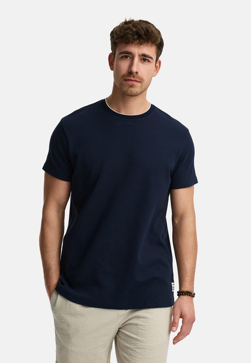 Camiseta de algodón azul marino con mangas cortas y cuello redondo, que presenta una textura sutil y una pequeña etiqueta de logo en el dobladillo inferior.