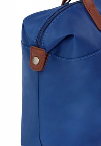 Borsa sintetica blu con dettagli in pelle marrone, chiusura a zip e finitura testurizzata. Presenta una maniglia robusta e un dettaglio unico della tasca.