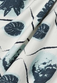 Stof met een bladpatroon in donkerblauw en lichtblauw op een witte achtergrond; gestructureerd oppervlak met zichtbare draden en printdetails.