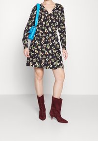 Czarna sukienka w kwiaty z długimi rękawami, warstwowy wzór w kolorach zielonym, białym i pomarańczowym. Do tego bordowe zamszowe botki do kostki i niebieska torebka.