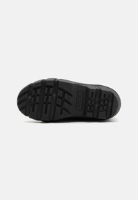 Suela de zapato de goma negra con un agarre texturizado, que presenta surcos profundos y un logo incrustado en la goma. Duradera y diseñada para proporcionar tracción.