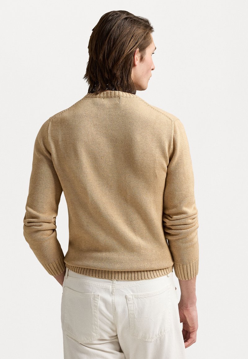 Beige gestrickter Pullover aus strukturiertem Stoff, Rundhalsausschnitt und gerippten Bündchen und Saum. Getragen mit hellen Hosen, die die Rückansicht zeigen.