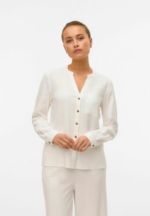Blusa bianca a maniche lunghe con chiusura a bottoni sul davanti, scollo a V e una tasca sul petto; realizzata in un tessuto leggero e strutturato.