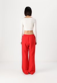 Un haut court à manches longues blanc et un pantalon large rouge avec une taille élastique. Tissu lisse et extensible avec une coupe décontractée.