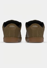 Καφέ σουέτ αθλητικά παπούτσια με μαύρη επένδυση στον αυχένα, διαθέτοντας μια καφέ λαστιχένια σόλα και το λογότυπο Etnies στη φτέρνα. Λείος υφασμάτινος σχεδιασμός και χαμηλή κοπή.