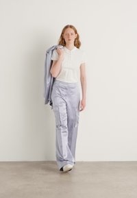 Lichtpaarse cargobroek met verticale strepen en zakken, gecombineerd met een aansluitend wit poloshirt. Een licht jasje hangt over één arm.