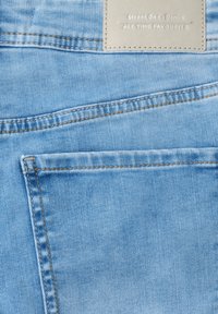 Jasnoniebieska tkanina jeansowa z widocznymi szwami oraz beżową metką z napisem „Street One Denim ALL TIME FAVOURITE” w pobliżu górnej krawędzi.