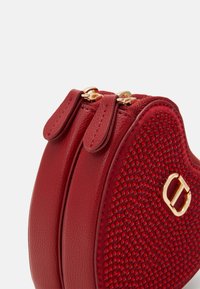 Borsa a tracolla rossa in pelle a forma di cuore, con frontale testurizzato, lati lisci, hardware dorato e doppie chiusure a zip.