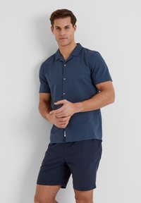 Navy short-sleeve shirt in textured fabric with a collar and three buttons. Paired with navy shorts, displaying a casual and fitted design.