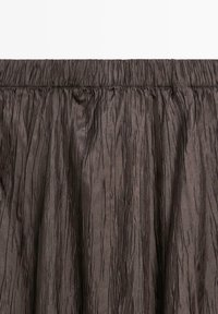 Jupe plissée marron foncé en tissu texturé, avec une taille élastique et des lignes verticales irrégulières pour plus de détail et de dimension.
