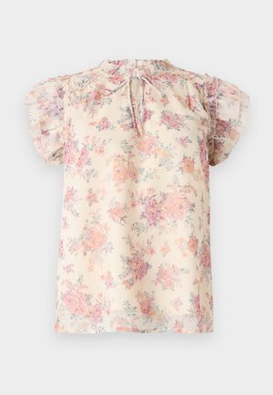 Blouse crème à motif floral rose et violet, manches courtes à volants, et petite ouverture en forme de goutte nouée par un nœud à l'encolure.