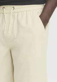 Pantalons de survêtement beige clair avec une taille élastique et un cordon de serrage. Comprend des poches latérales et un tissu doux et texturé.