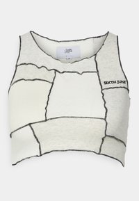 Weißes Cropped-Top aus weichem Stoff mit kontrastierendem schwarzen Nähten. Es hat ein Patchwork-Design und einen runden Halsausschnitt mit einem Etikett.