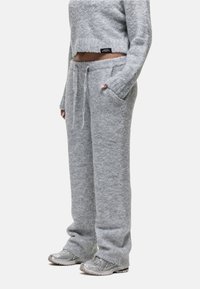 Persoon in grijze, fuzzy textuur sportbroek met trekkoord, bijpassende cropped sweater en zilveren sportschoenen, staand met één hand in de zak.