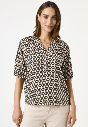 Blusa de manga corta en una tela color crema con un patrón geométrico negro, que presenta un escote en V y detalles fruncidos en los hombros.