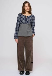 Kockás hosszú ujjú felső összehúzott nyakkivágással és mintás peplummal; széles, barna kordnadrággal és fekete fűzős cipővel párosítva.