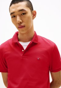 Κόκκινο πόλο πουκάμισο από βαμβάκι, με κλασικό γιακά, εμπρόσθιο άνοιγμα με δύο κουμπιά και μικρό κεντημένο λογότυπο στο αριστερό στήθος.