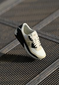 Nike Air Max sneeker kreemjas, mustas ja kuldsetes toonides. Omab nahkpealist, tekstuurset külgpaneeli ja pehmendatud tallat, kus on nähtav õhuühik.