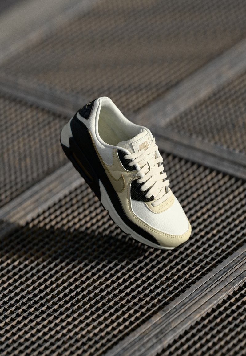 Nike Air Max sneeker kreemjas, mustas ja kuldsetes toonides. Omab nahkpealist, tekstuurset külgpaneeli ja pehmendatud tallat, kus on nähtav õhuühik.