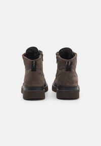 Botine din suede maro, cu un finisaj texturat, dotate cu fermoar pe fiecare botină și o talpă solidă neagră. Detalii discrete ale brandului pe toc.