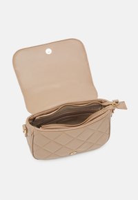 Beige quiltad syntetväska med dragkedja på insidan och tryckknappsstängning; har detaljer i guldton och en slät yta.