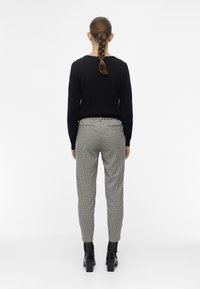 Un haut noir à manches longues associé à un pantalon ajusté à carreaux gris et noirs. La tenue est complétée par des bottines noires à talons.