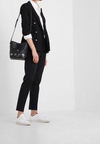 Svart dubbelknäppt kavaj med silverknappar, vit skjorta, svarta skräddarsydda byxor och vita sneakers; svart bucket bag med silveröglor.