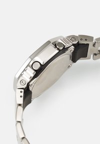 Metal watch with a brushed silver stainless steel case, black silicone band, side buttons, and a smooth round rear.