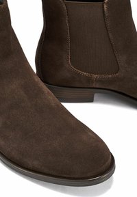 Brązowe zamszowe botki za kostkę z elastycznymi panelami bocznymi, zaokrąglonym noskiem i niskim, warstwowym obcasem z subtelnymi detalami w postaci przeszyć.