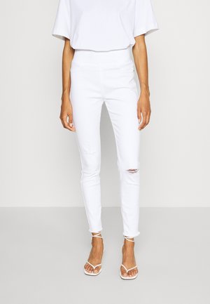 Hvide skinny jeans med høj talje og et slidt knæ. Bæres med en løs hvid top og strop-sandaler i hvid.