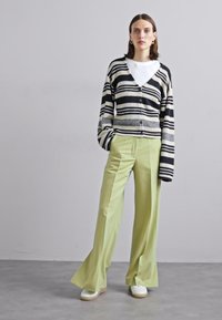 Gestreepte cardigan in zwart en wit met grijze accenten, gecombineerd met lichtgroene wijde broek en witte sneakers. Zachte textuur, ontspannen pasvorm.