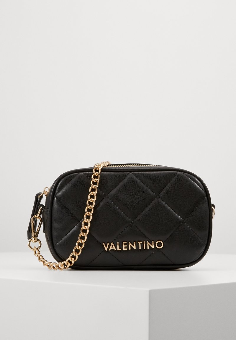 Black quilted leather crossbody bag with gold hardware, featuring a chain strap and embossed brand name on the front, rectangular shape.