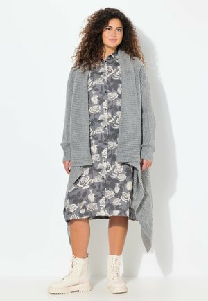 Cardigan en maille grise sur une robe chemise florale grise et blanche, assortie à des bottines lacées ivoire ; les textures créent un contraste dans la tenue.
