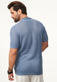 Helles blaues gestricktes Poloshirt mit atmungsaktivem, offenem Strickmuster, kurzen Ärmeln sowie geripptem Kragen und Bündchen.