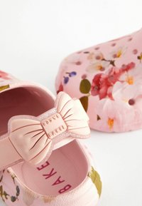 Chaussures à enfiler roses à motif floral avec un accessoire nœud pailleté amovible embossé du mot "BAKER" sur fond blanc.