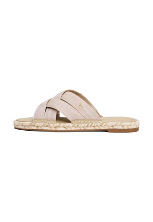 Beige platte sandaal met gekruiste stoffen bandjes en gevlochten jutezool tegen een witte achtergrond.