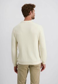 Cremefarbener, gerippter Pullover mit langen Ärmeln und Kragen. Kombiniert mit hellen Hosen. Dezente Textur im gesamten Stoff.