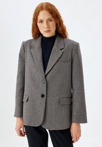 Blazer imHahnentrittmuster in Grau, Schwarz und Rot. Mit Eingriffstaschen, zwei Knöpfen und einem Reverskragen. Strukturierter, taillierter Schnitt.