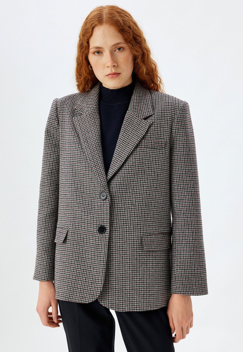 Blazer imHahnentrittmuster in Grau, Schwarz und Rot. Mit Eingriffstaschen, zwei Knöpfen und einem Reverskragen. Strukturierter, taillierter Schnitt.
