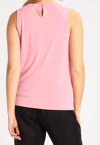 Top senza maniche di un rosa chiaro con dettaglio a bussola sul retro, realizzato in tessuto morbido. Design semplice con vestibilità rilassata, abbinato a pantaloni neri.