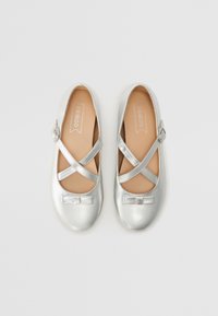 Scarpette da balletto metalliche argento con cinturini incrociati e un dettaglio a fiocco sulla punta. Materiale liscio con una fodera interna beige.