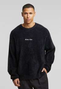 Suéter negro de felpa con cuello redondo, mangas largas y logo bordado "Another Cotton" en el pecho, que presenta un corte holgado y una textura suave.
