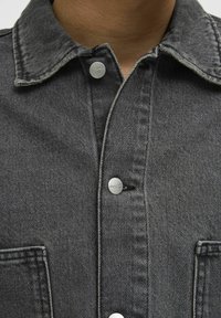 Sötét denim dzseki, gombos elejével, hegyes gallérral és mellzsebbel. Kontraszt varrásokkal és ezüstszínű fém részletekkel.