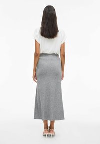 Jupe longue en tricot gris avec une taille ajustée, associée à un haut à manches courtes blanc. Le tissu semble doux et lisse, tombant délicatement.